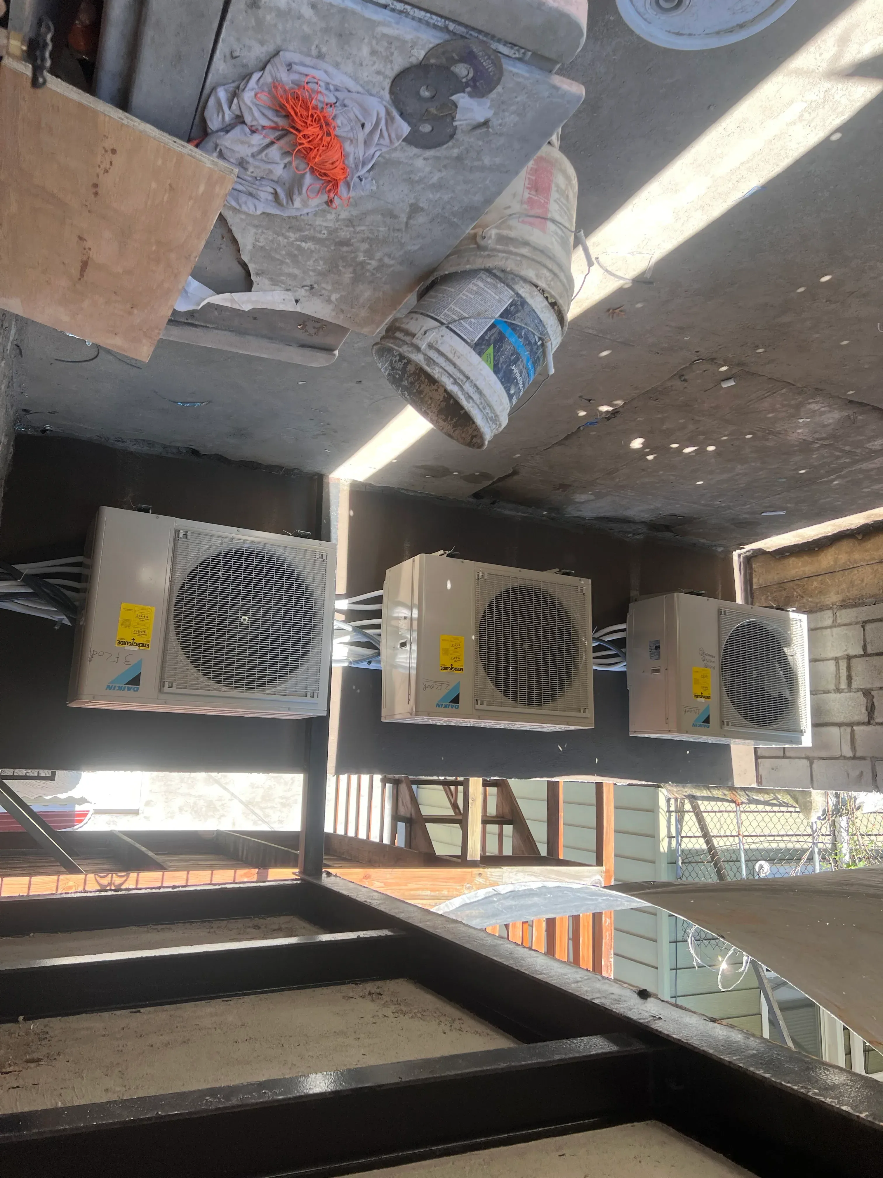 Three outdoor AC condenser units installed on building platform with refrigerant lines