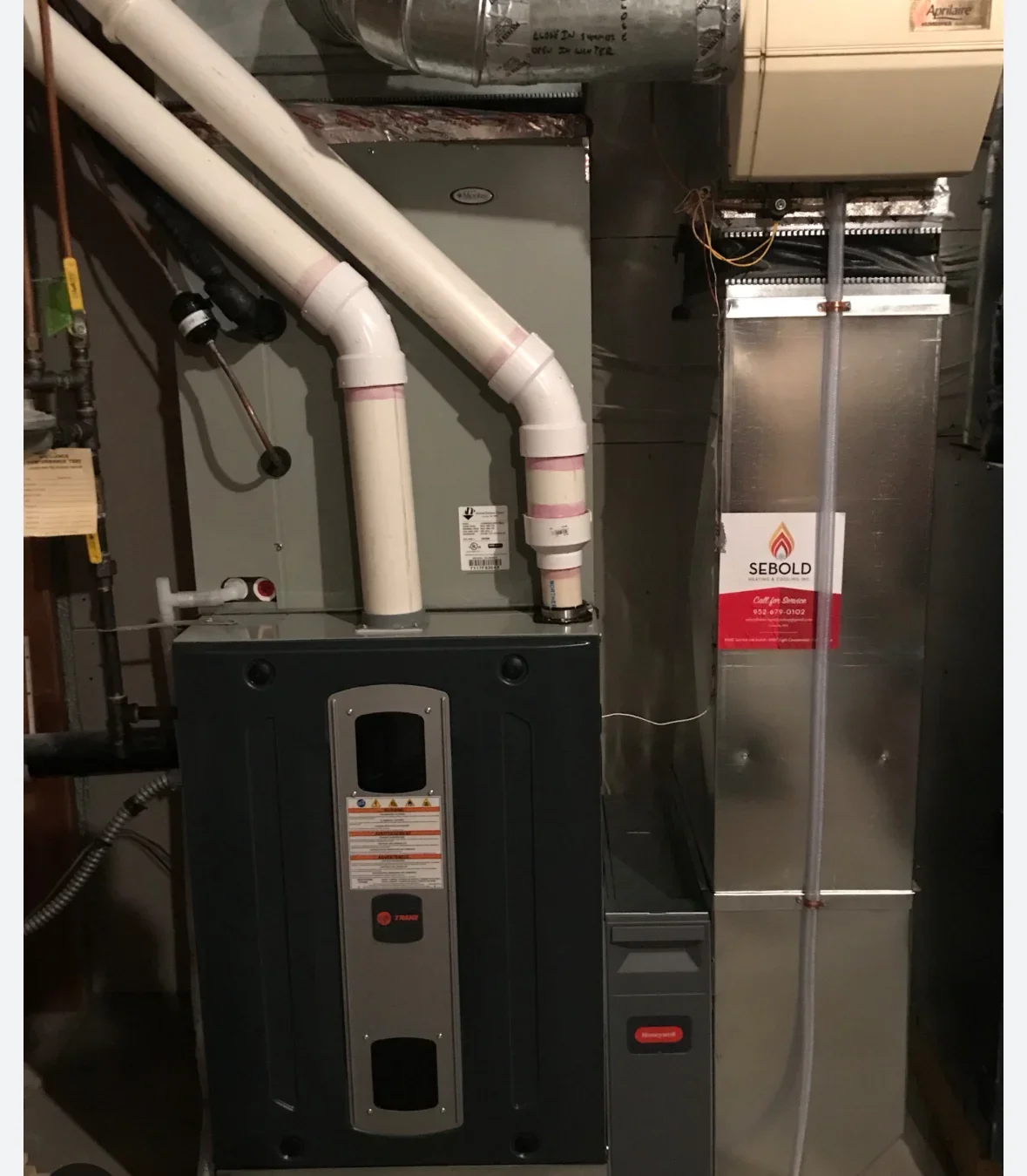 Installed furnace and water heater with white ductwork and electrical panel in utility room