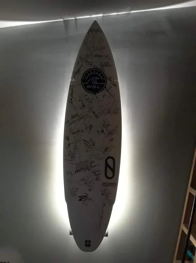 White surfboard with WSL logo and signatures mounted on wall with LED accent lighting