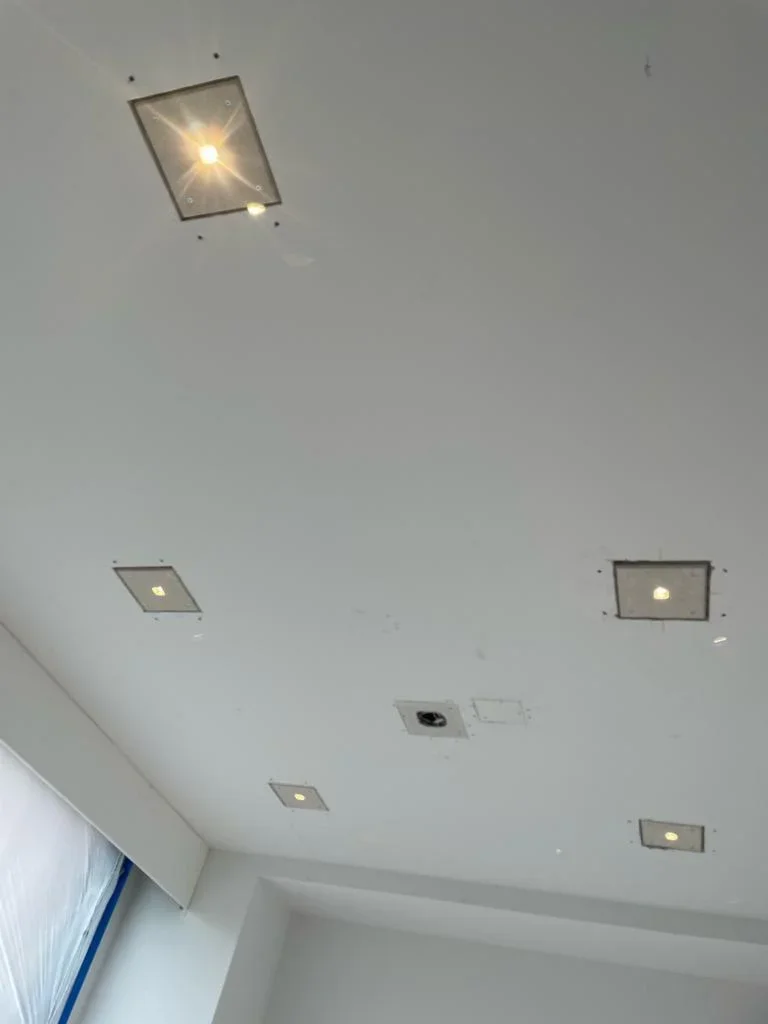 Five recessed ceiling lights installed in white drywall with metal trim rings