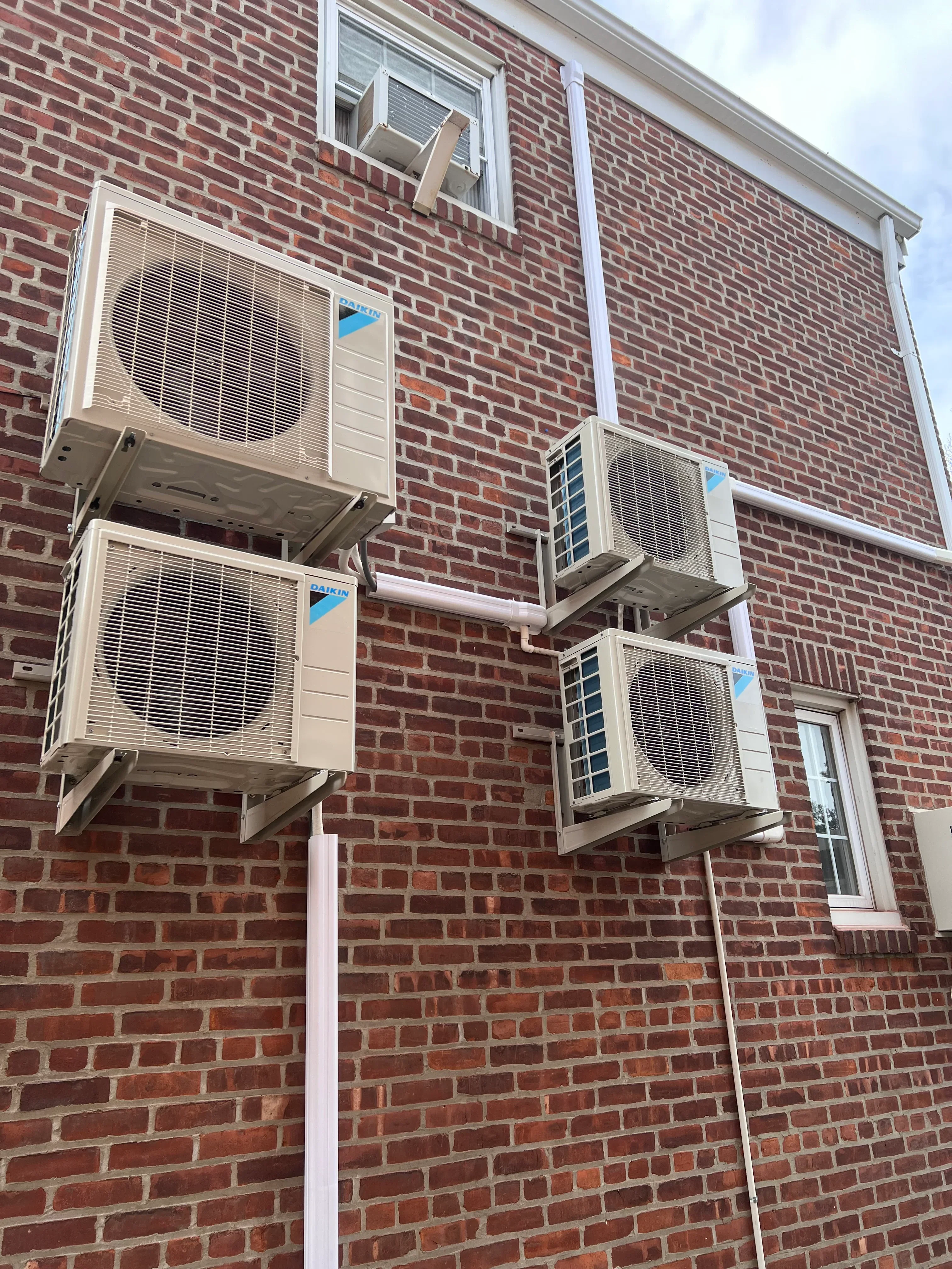 Four AC condenser units installed on red brick building exterior in Bayside