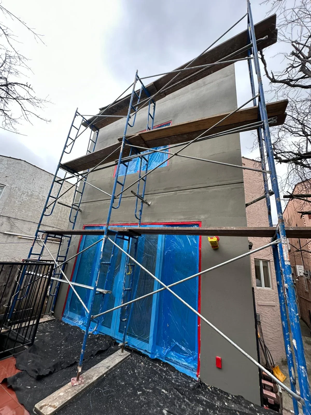 Multi-story building facade under renovation with blue scaffolding and protective sheeting